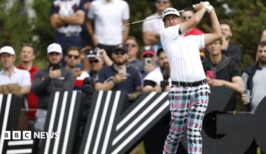 Ian Poulter in the middle of a follow-through after hitting a shot during a professional tournament. In the background are large black signs featuring bold white striped graphics.