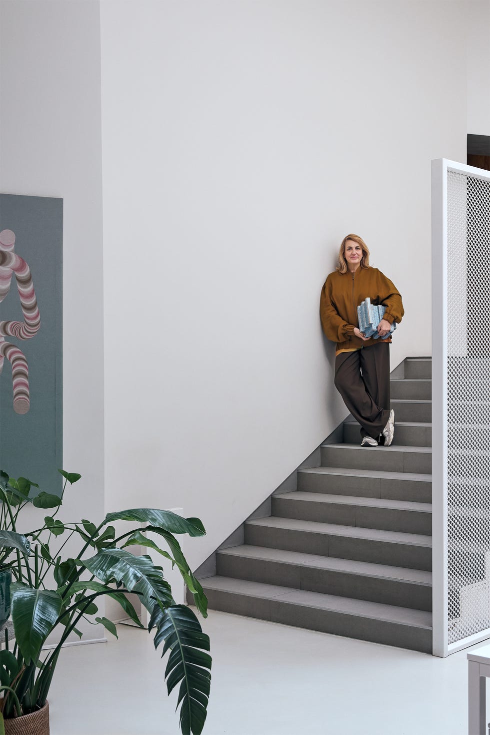 Person standing on a modern staircase holding books, next to a large plant.