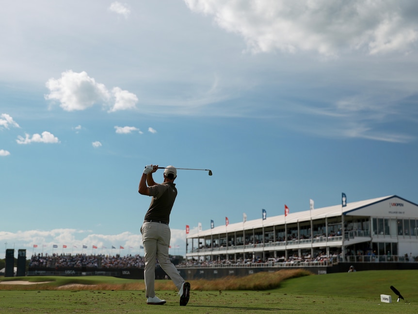 A wide shot from behind of a golfer hitting a tee shot.