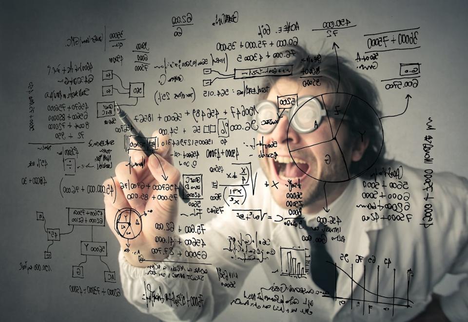 A person in thick glasses and a lab coat writes a complicated equation on a transparent board.