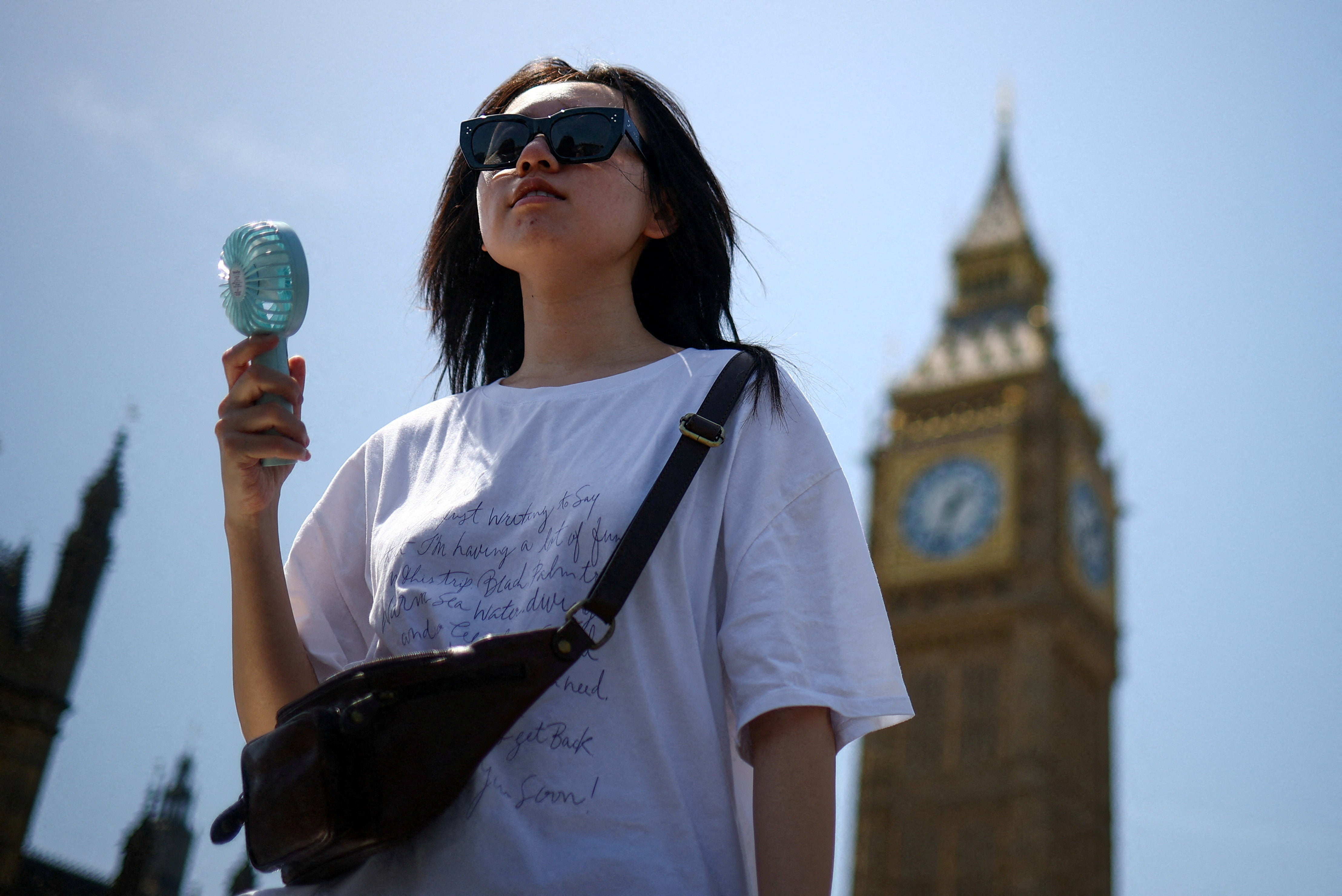 A woman uses a fan as she walks near the Houses of Parliament, amid hot weather in London