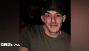 Rob Campbell has dark stubble, a black hat and khaki T-shirt