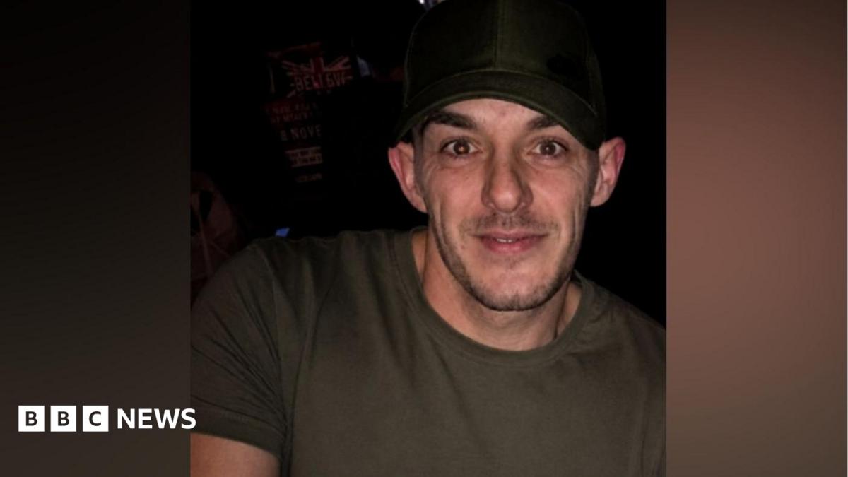 Rob Campbell has dark stubble, a black hat and khaki T-shirt