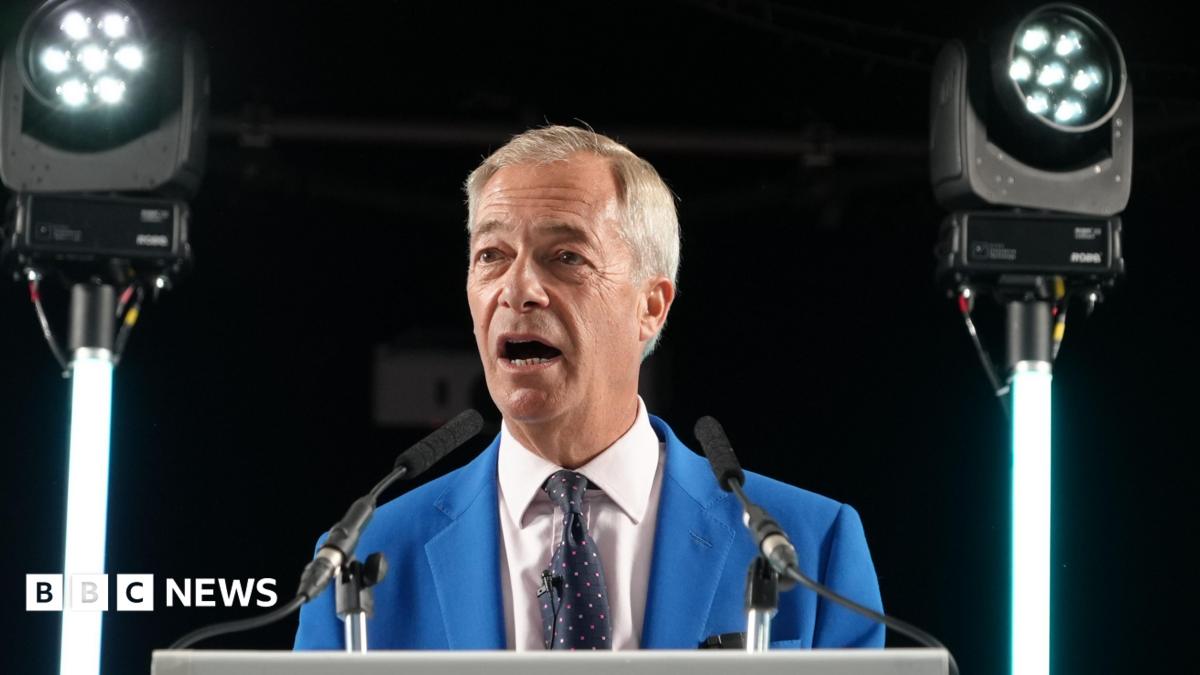 Nigel Farage in a bright blue suit, white shirt and black tie, with red and white coloured dots stands behind a lectern. Two lights are either side of him.