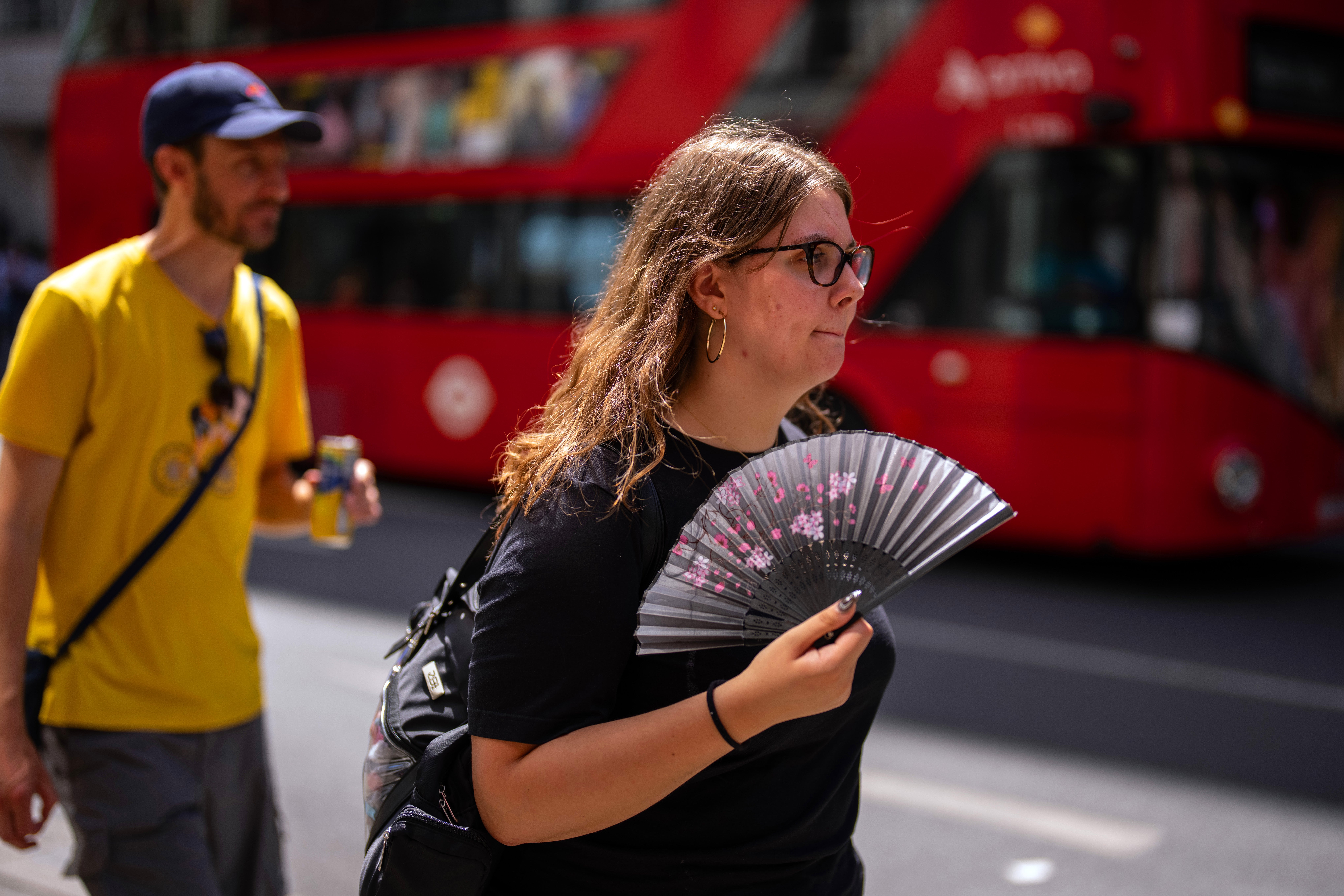 A woman uses a fan to cool herself as she walks through central London in the hot weather