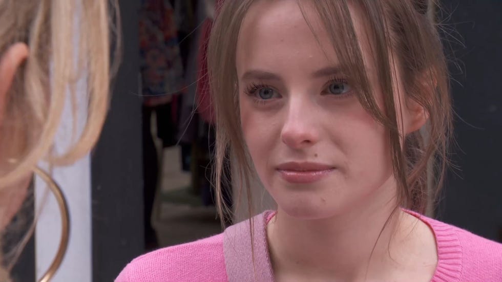 Hollyoaks, Leela Lomax and Dee Dee Hutchinson hollyoaks, close up of dee dee hutchinson in a pink cardigan giving an intense glare to leela lomax, who is seen from behind on the left hand side of the image