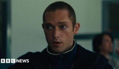 Sonny Walker, who is playing the role of Paul in Legends, is staring off camera in this still from filming. He has a buzz cut and is wearing a jumper with a coat over the top.