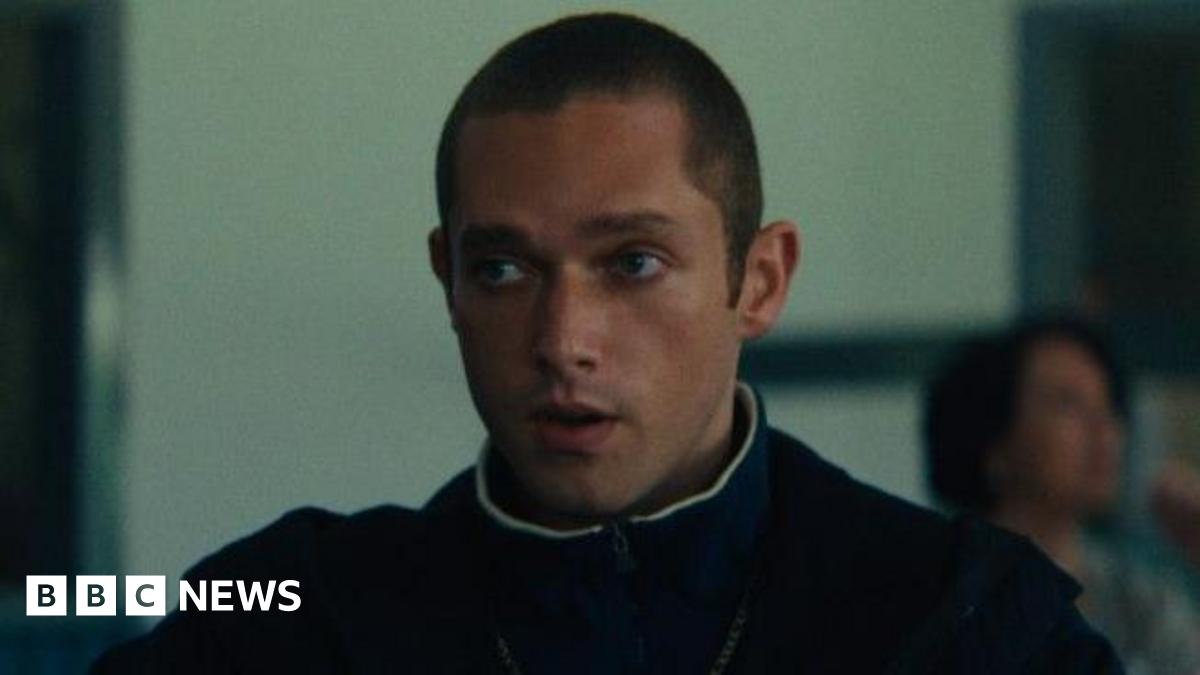 Sonny Walker, who is playing the role of Paul in Legends, is staring off camera in this still from filming. He has a buzz cut and is wearing a jumper with a coat over the top.