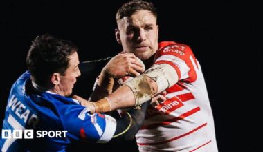 St Helens prop forward Matty Lees, in red and white, fends off Workington Town player Dom Wear, in blue and white.