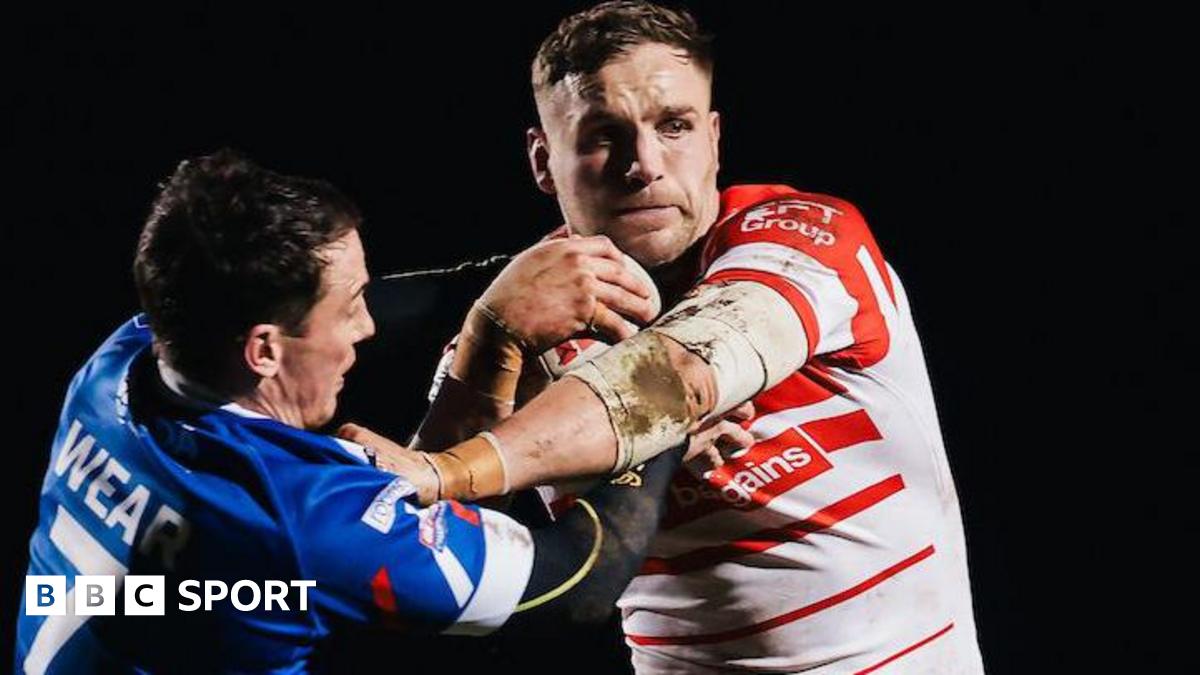 St Helens prop forward Matty Lees, in red and white, fends off Workington Town player Dom Wear, in blue and white.