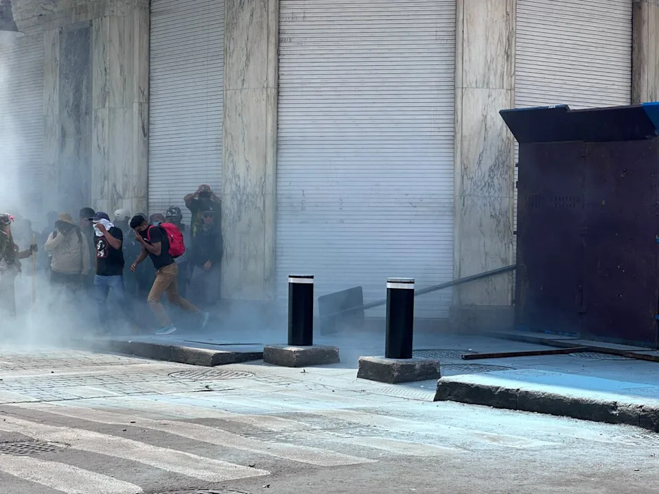 Protestors run from smoke launched by Mexico City policy from behind metal barricades on June 1, 2026.
