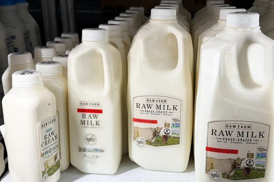 Bottles of raw milk and cream from Raw Farm, showcasing various sizes, are displayed on a shelf