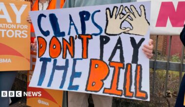 A group of people striking, one has a banner that says claps don't pat the bill.