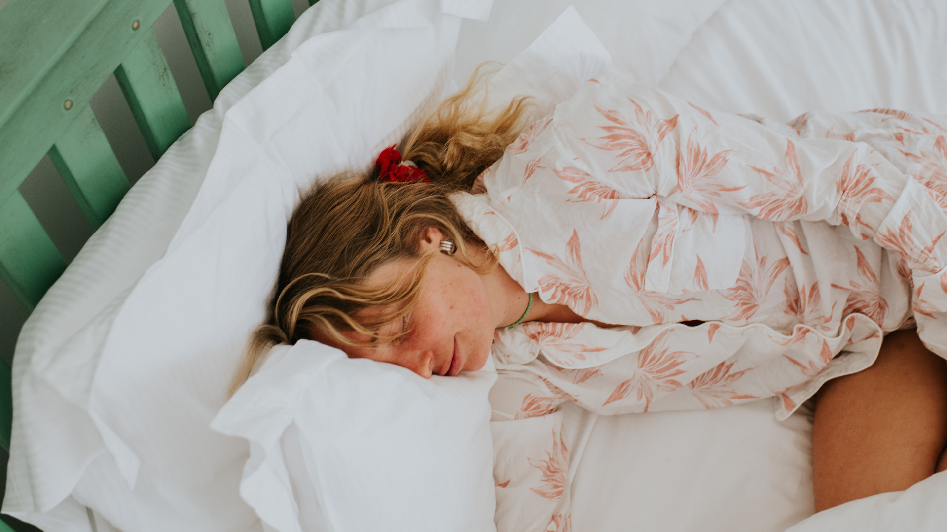 A woman sleeping on her side in bed in the morning, she is wearing light red and white patterned pajamas.