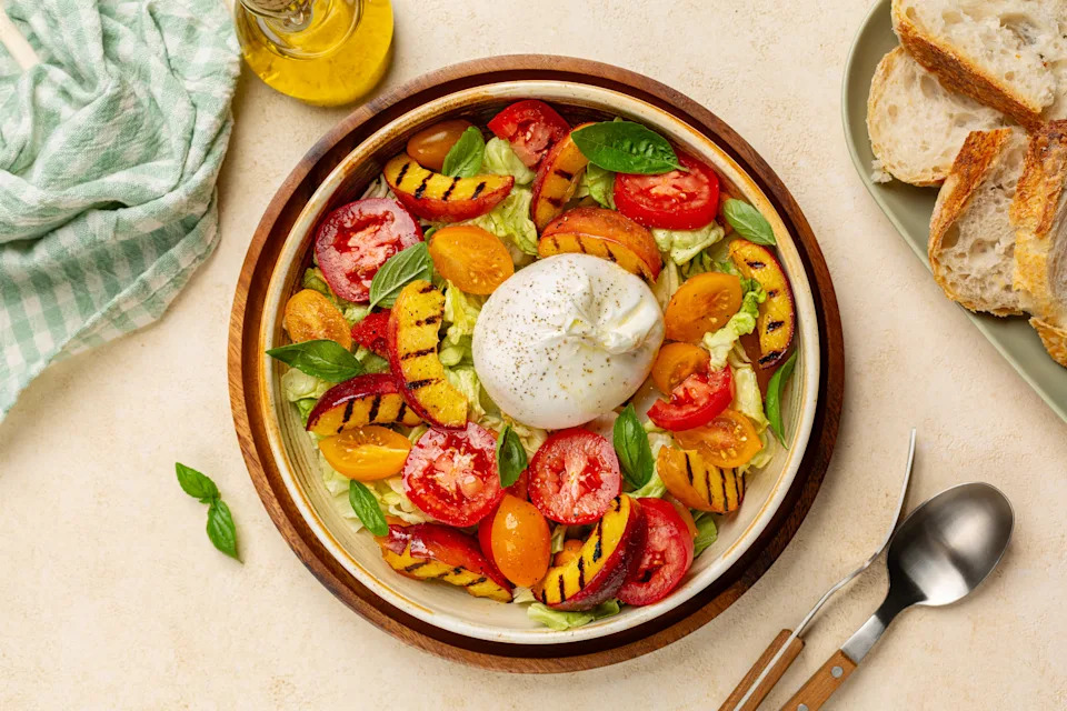 Summer salad with grilled peaches, tomatoes and burrata cheese, dressed with olive oil. Fresh Bread. Top view.