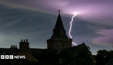 Dornoch Cathedral under the night sky. It is dark and there is a lightning bolt in the purple-coloured sky.