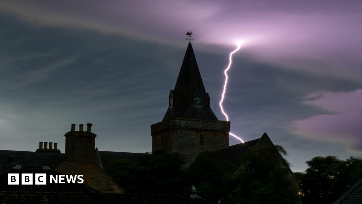 Dornoch Cathedral under the night sky. It is dark and there is a lightning bolt in the purple-coloured sky.