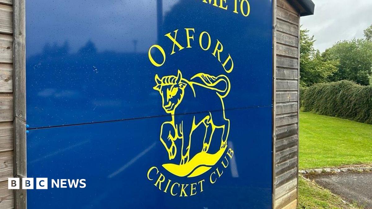 A blue sign with the Oxford Cricket Club logo, which is an ox, in yellow.