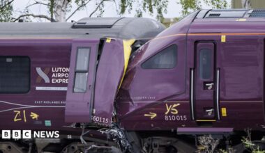 Two trains that have collided. One train is badly damaged. The driver's cab is crumpled and twisted.