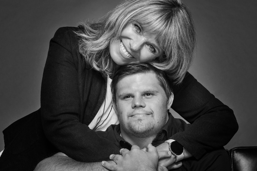 A black and white studio portrait shows a woman with her arms around her son.