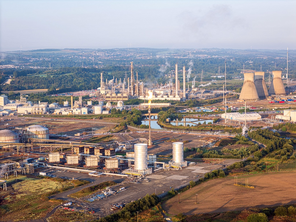 Aerial view of industrial complex with towering chimneys and storage tanks under a hazy sky, Grangemouth, Scotland, United Kingdom.