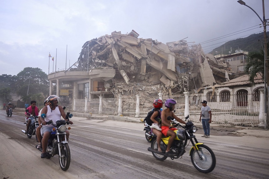 People on motorcycles drive past an enormous pile of rubble