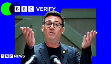 Andy Burnham holds his hands up in front of him as he delivers a speech