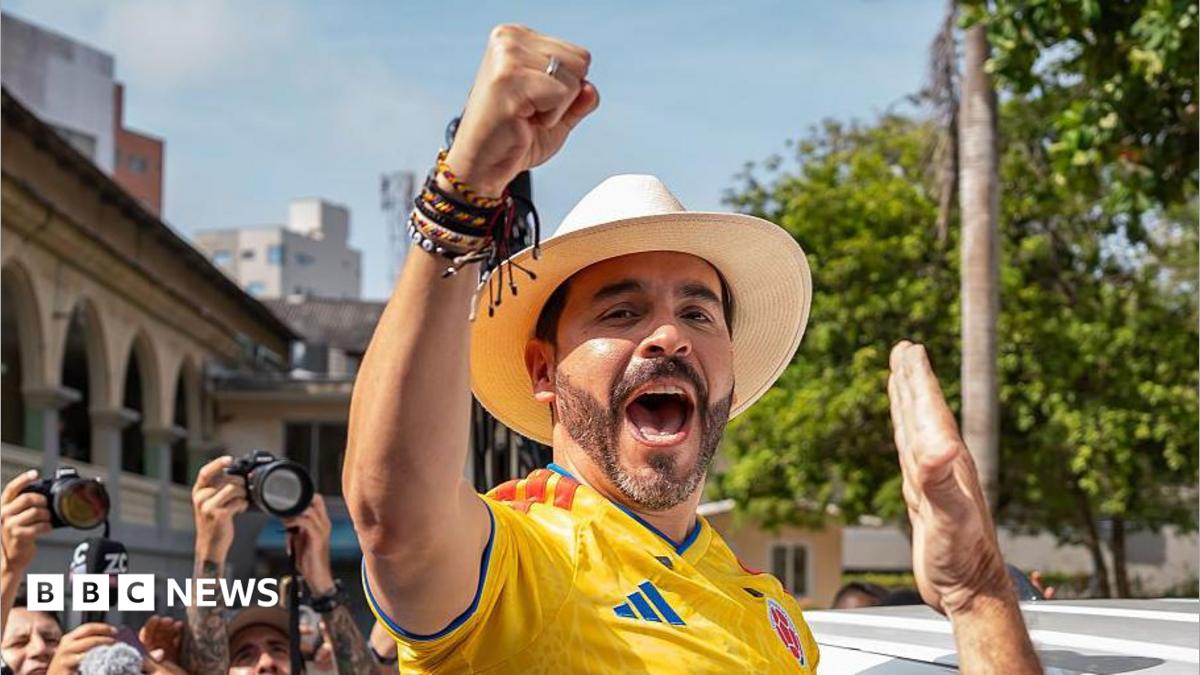 Abelardo de la Espriella cheers, wearing a hat and football shirt.