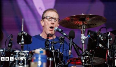 A man, Dave Rowntree, playing drums on a stage.
