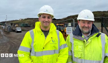 Douglas button (left) and Robert Roussel wearing green high visibility coats. Behind there are big hills. The are both wearing white Guernsey Waste hats.