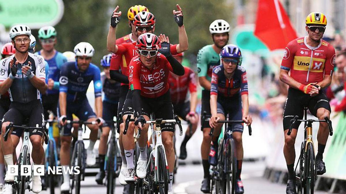 Geraint Thomas crosses the finish line cheered by the riders in his farewell and last race as a professional cyclist during the 21st Tour of Britain 2025. The riders are all wearing cycling colours and helmets.