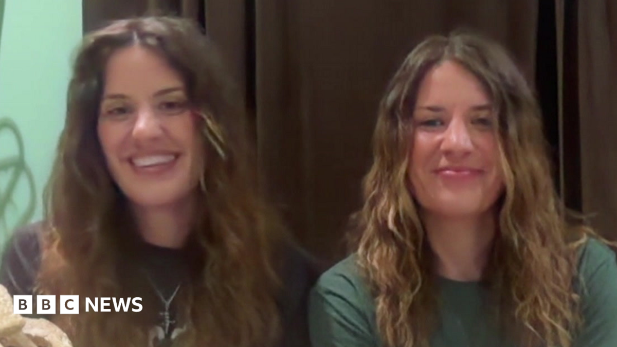 Georgia and Melissa Laurie, both sat in front of a webcam, smiling for the camera as they speak during an interview with BBC Breakfast. They both have long, brown or brown/blonde hair. Georgia is wearing a black T-shirt and Melissa a green T-shirt.