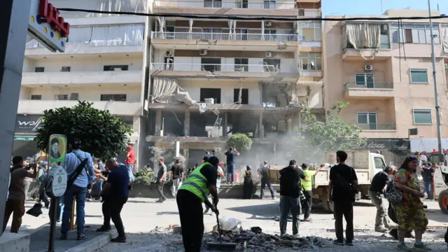 People clean up near the site of an apartment targeted by an Israeli airstrike in Beirut's southern suburbs, Lebanon