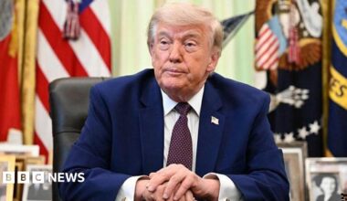 Donald Trump in the Oval Office wearing a Navy suit, white shirt and tie.