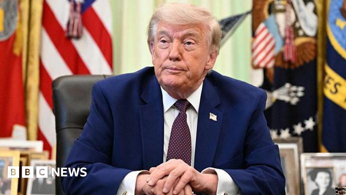 Donald Trump in the Oval Office wearing a Navy suit, white shirt and tie.