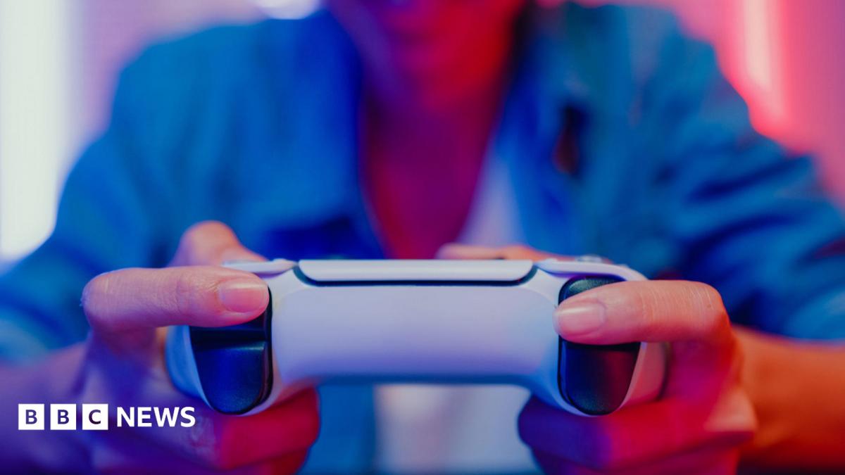 Close up of a woman's hands gripping a gaming controller, with colourful lighting reflecting on her from a monitor screen in front.
