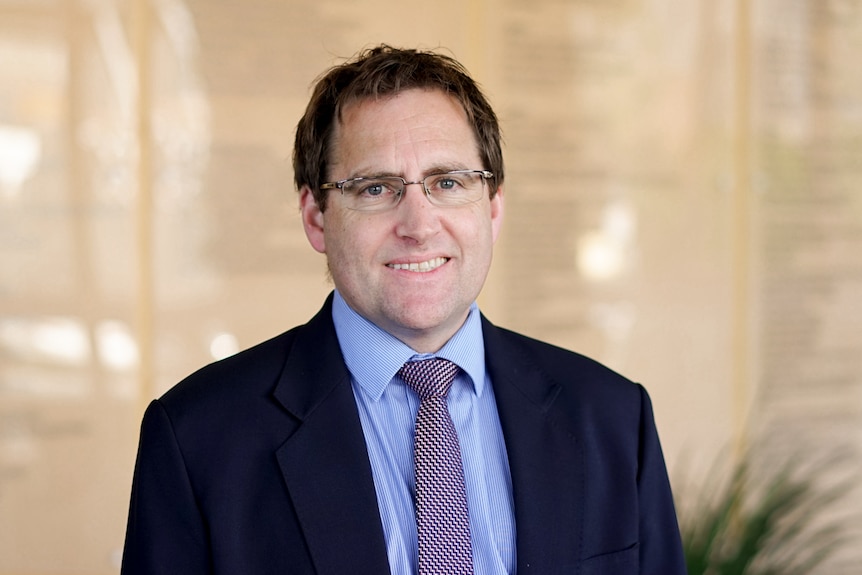 A man in a dark suit wearing glasses smiling at the camera