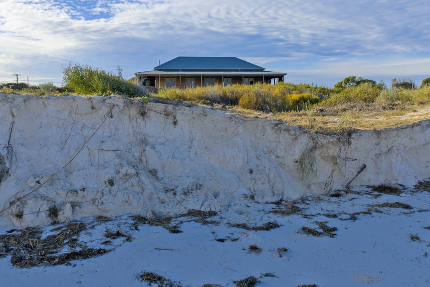 A steep drop in a sand dune, with a house in the background.