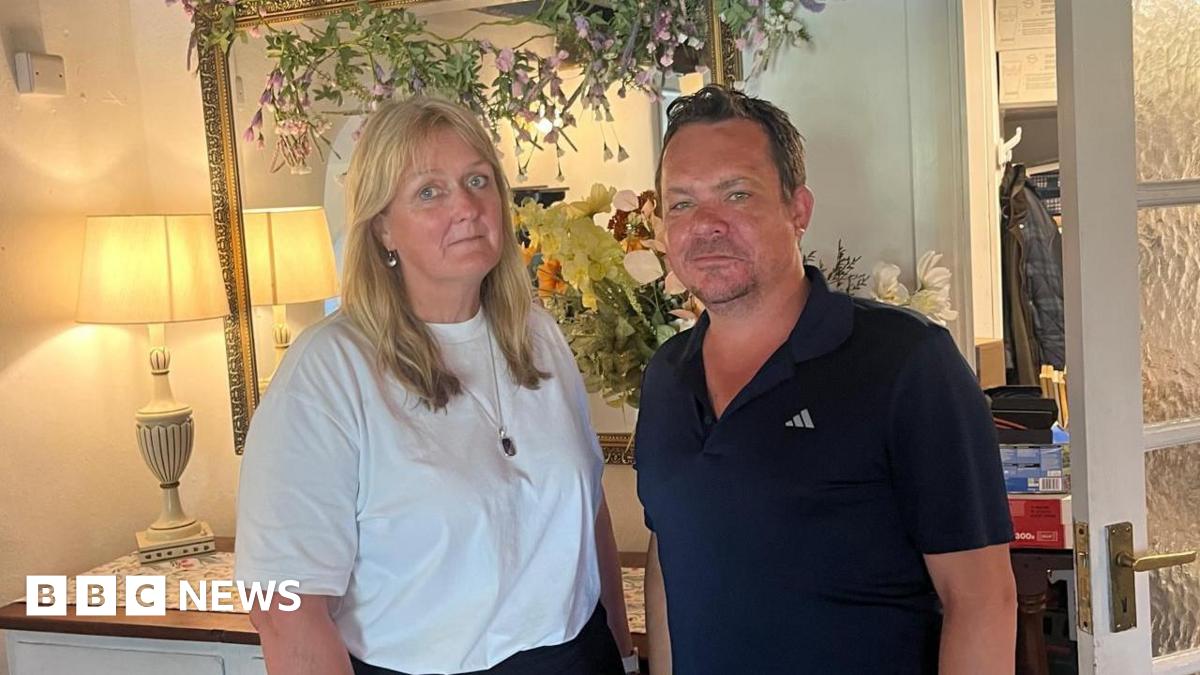 A women wearing a white t-shirt stood with a man wearing a blue polo shirt. They are both looking at the camera.
