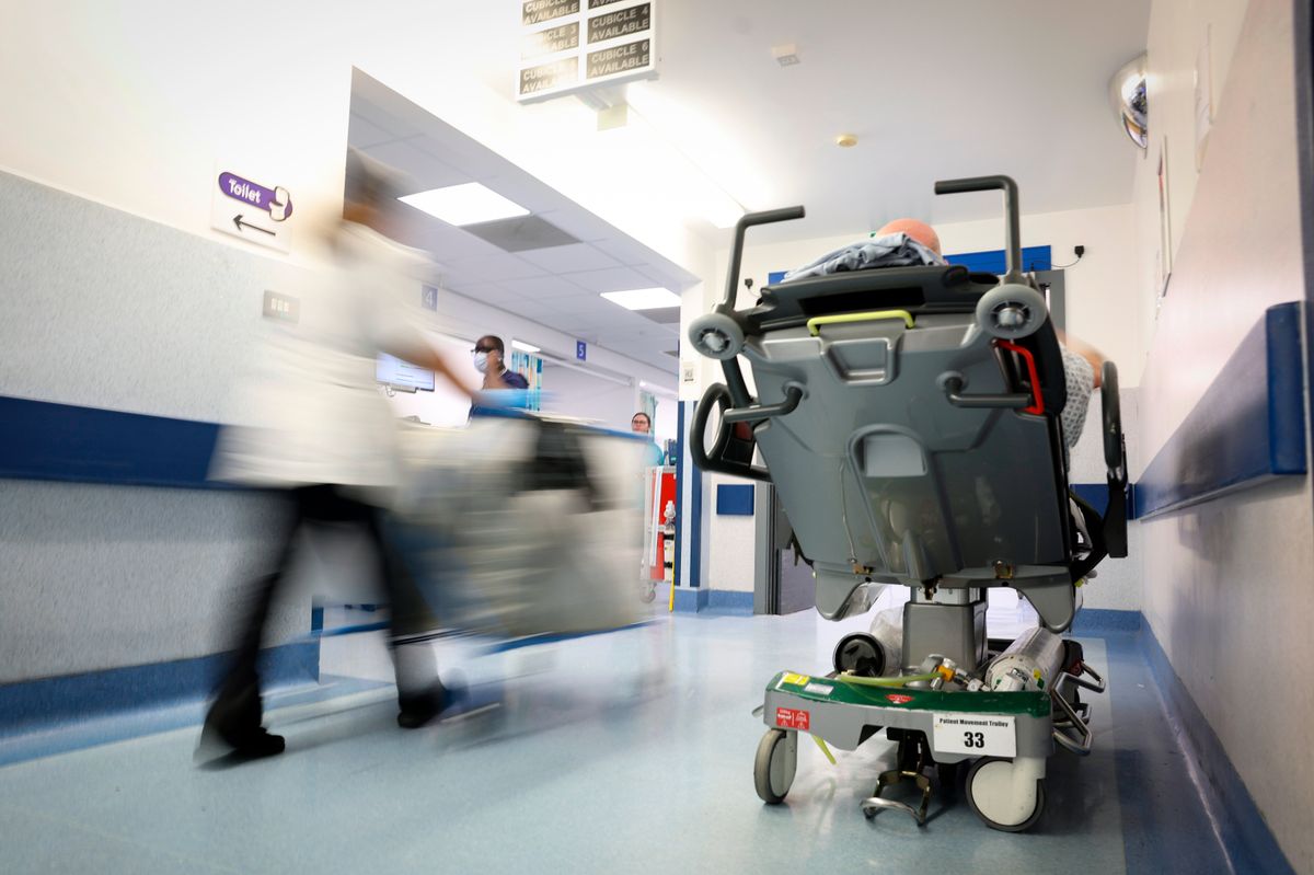 A staff member passes a patient on a bed in a corridor in the Emergency Department.