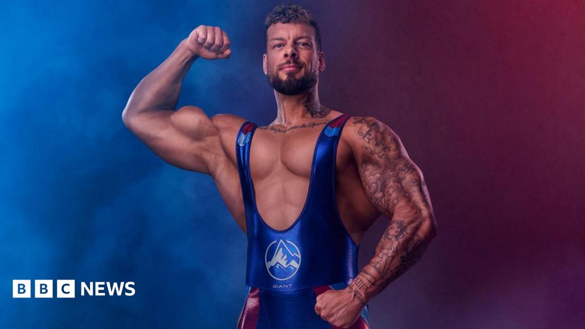 A man with extremely large biceps flexes his muscles in a blue and red leotard.