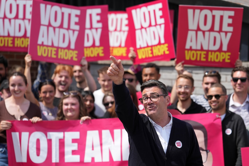 Andy Burnham pointing up and away, with a group of supporters behind him holding 'Vote Andy' placards.