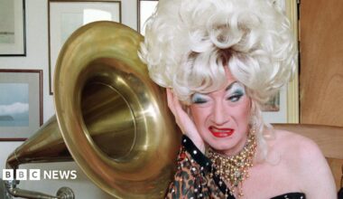 Paul O'Grady as his alter ego Lily Savage in a blonde wig next to a grammarphone