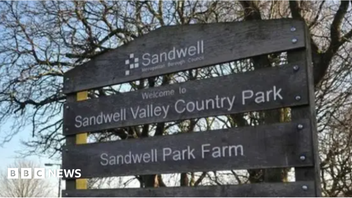 A mainly dark sign that includes the words Welcome to Sandwell Valley Country Park. Trees and grass are in the background.