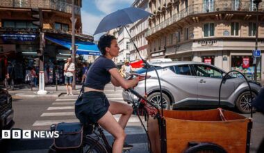 A woman protects herself from the sun under an umbrella as she rides a bicycle in Paris on June 25, 2026, as France experiences a heatwave.