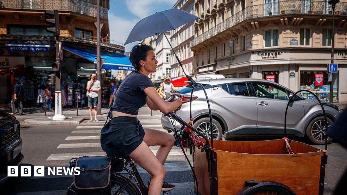 A woman protects herself from the sun under an umbrella as she rides a bicycle in Paris on June 25, 2026, as France experiences a heatwave.