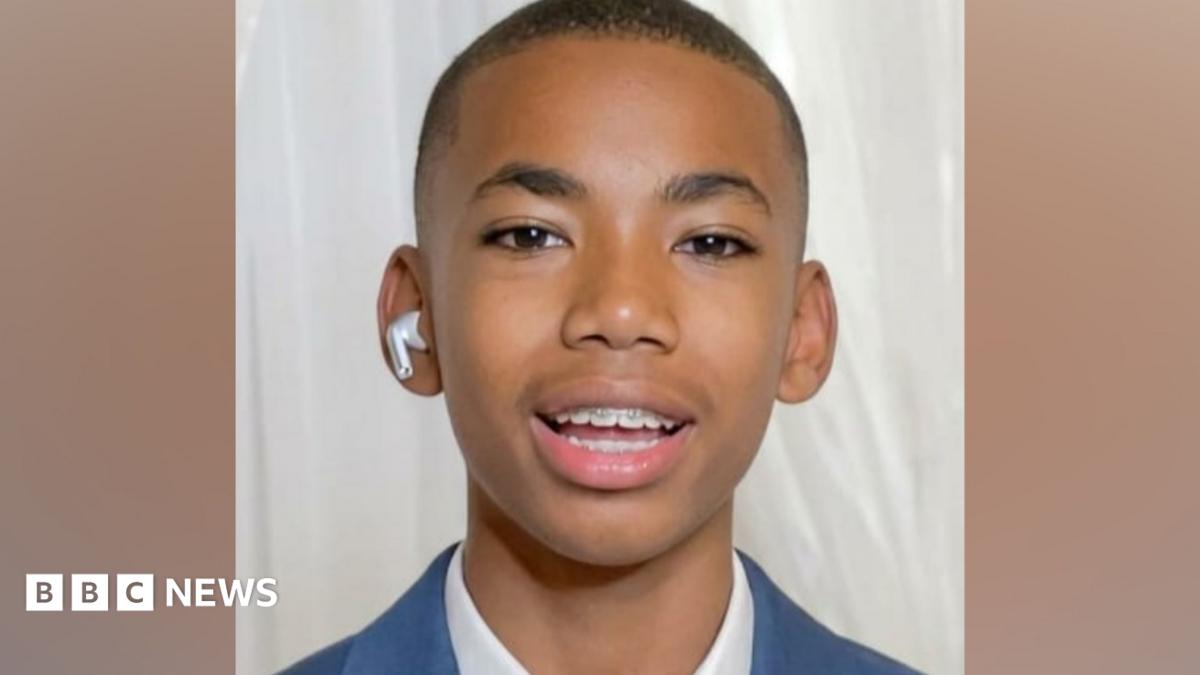Head shot of Jamal Coombes who is wearing a white shirt beneath a blue jacket. He has a white air pod in one ear