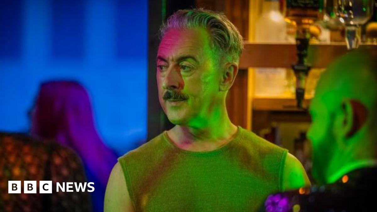 Alan Cumming is standing behind the bar during a scene from the filming of Tip Toe. Bottle