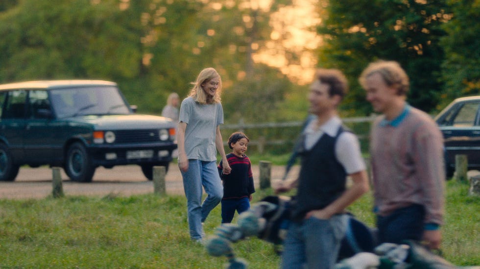 a woman and child walking in a grassy area with people in the background