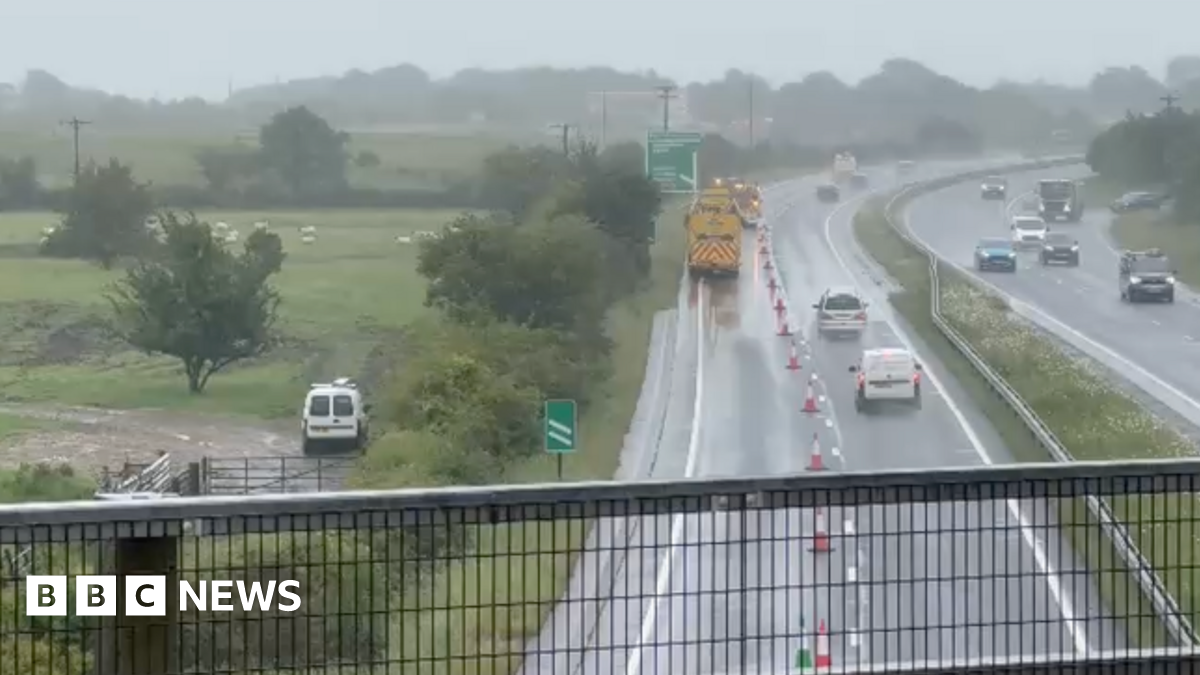 Cars drive down the A30 in Devon. One lane is closed off towards the exit slip road at Sourton Cross, near Okehampton. It is wet.